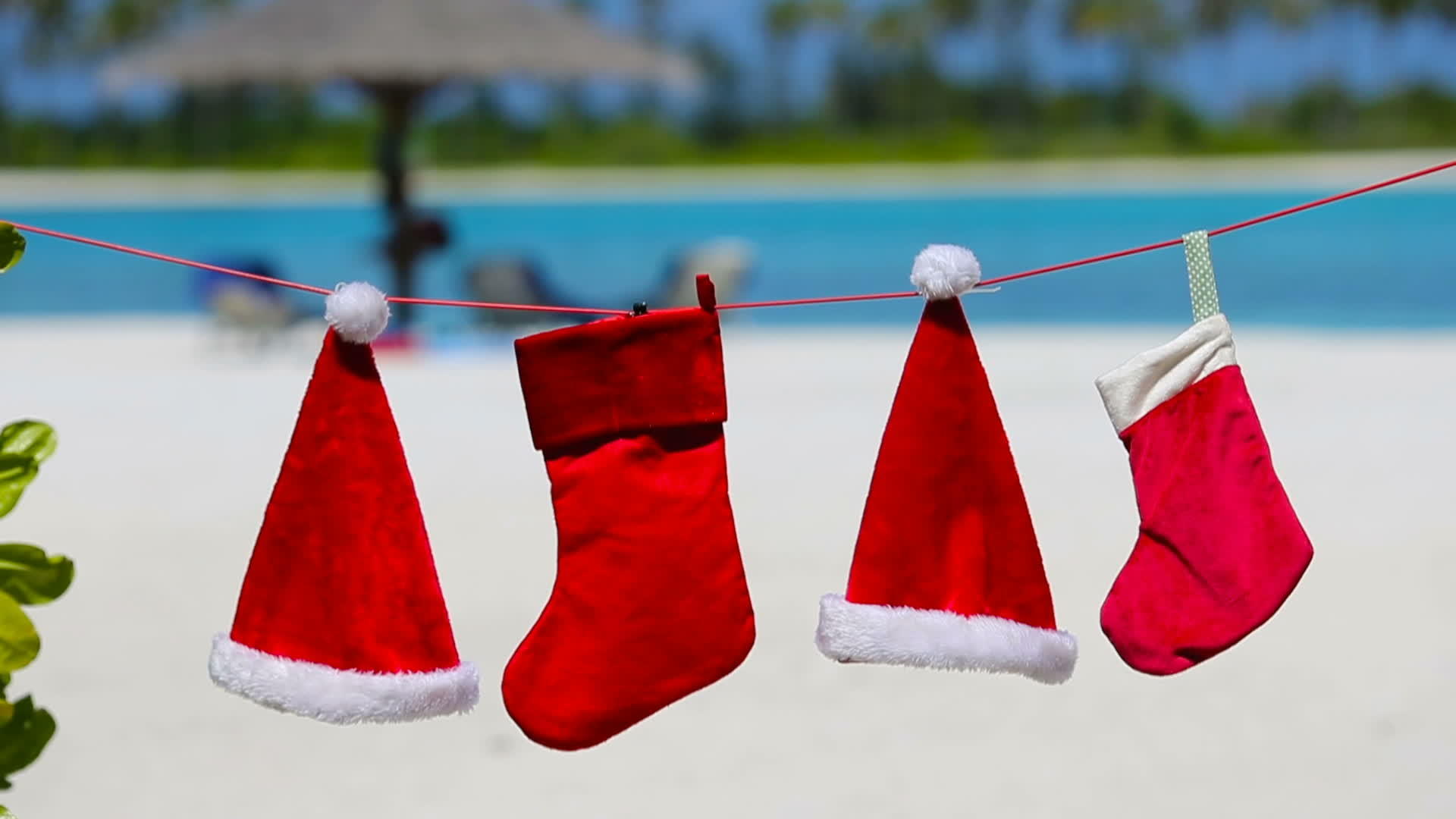 红色圣塔帽和圣诞长袜挂在热带海滩上视频的预览图