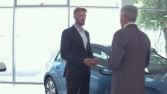 汽车展厅的年轻人与汽车经销商交谈视频的预览图