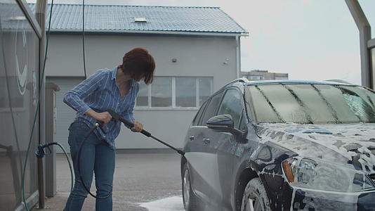 30岁的年轻女性在自助洗车时清洗家用汽车外面洗车视频的预览图