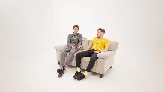 两个朋友坐在白色背景上在孤立的沙发上交谈或争论两个年轻人视频的预览图