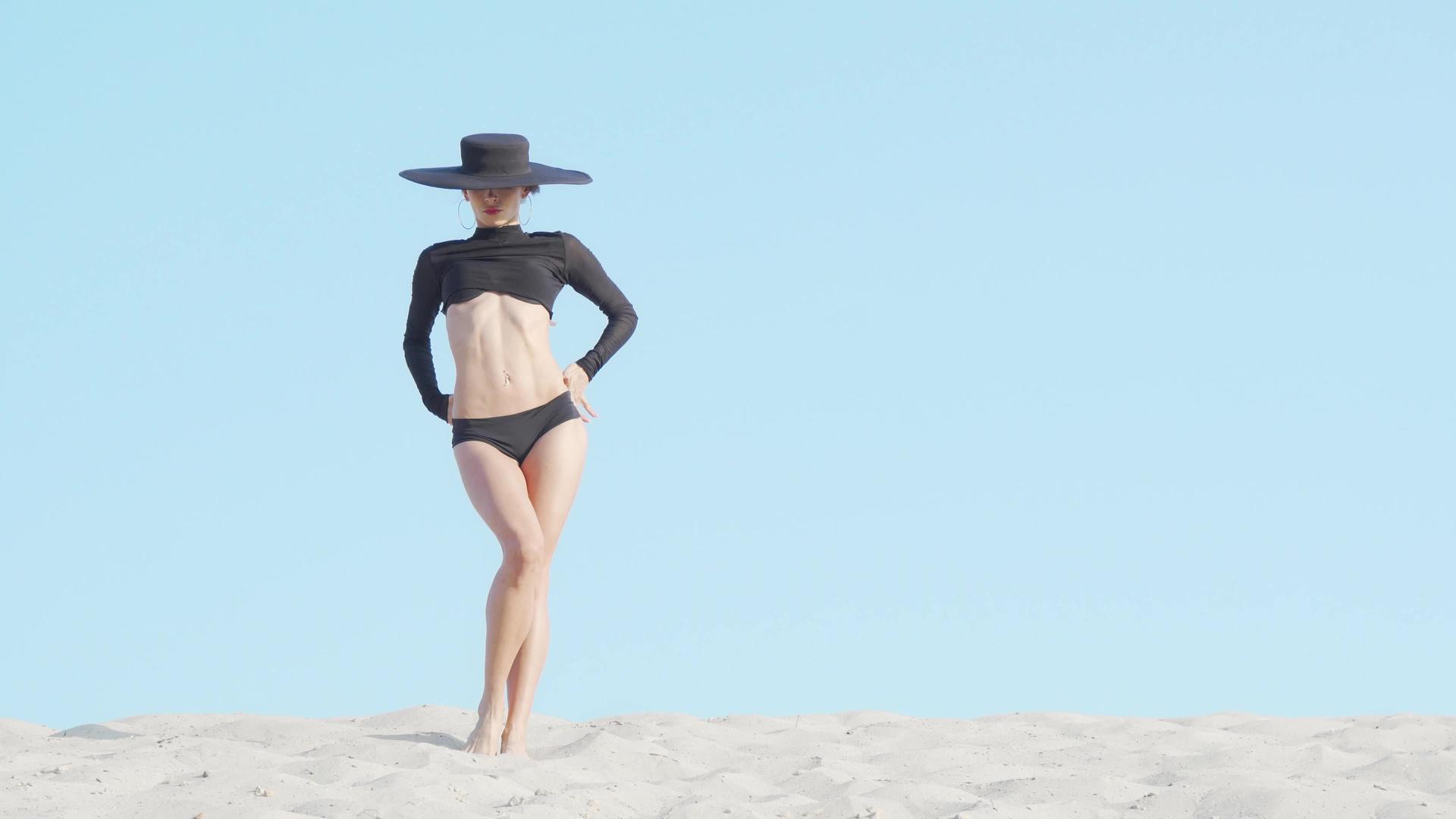 美丽优雅的女人戴着大黑帽子在沙滩上跳舞视频的预览图
