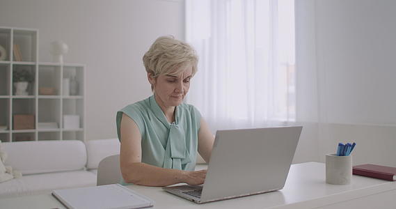 中年金发女子通过笔记本电脑在社交网络上使用互联网键盘视频的预览图