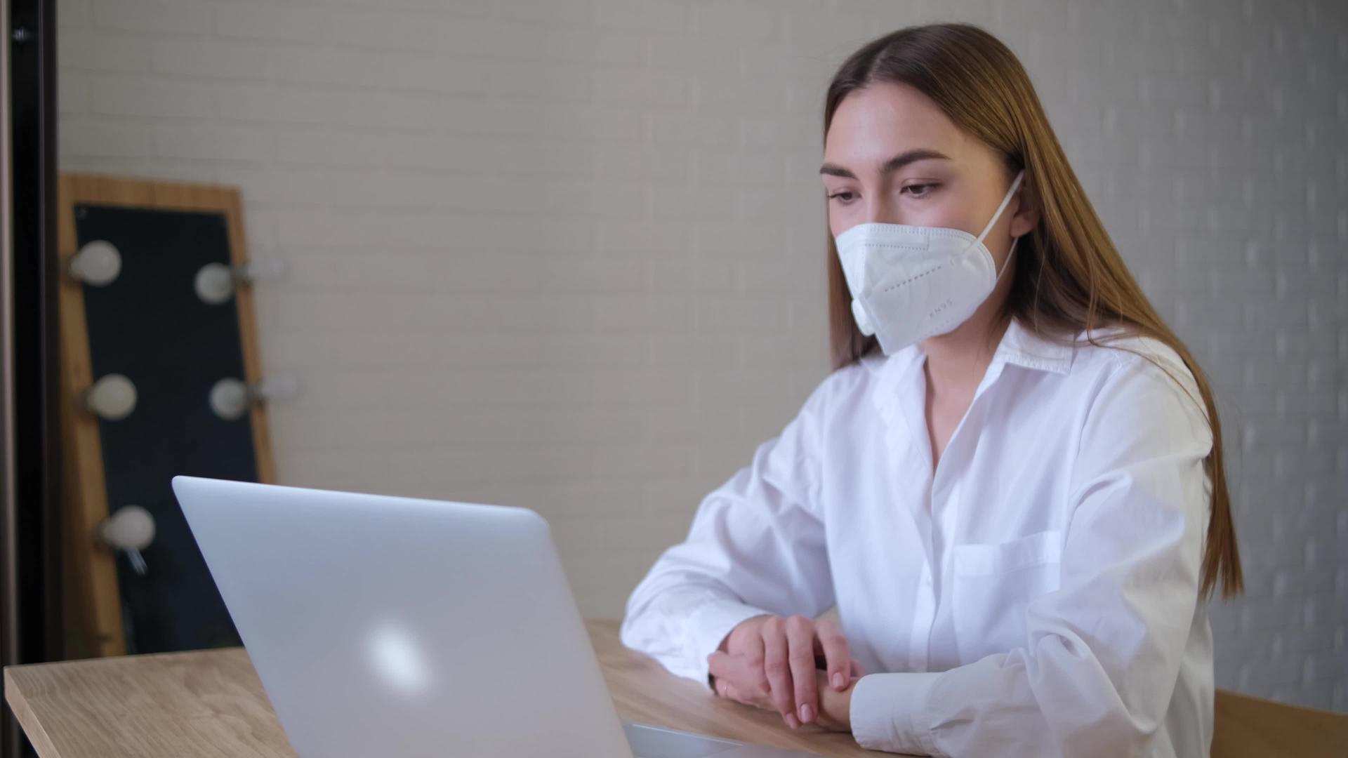一名戴着医用口罩的远程员工使用从家庭办公室开始的应用程序视频的预览图