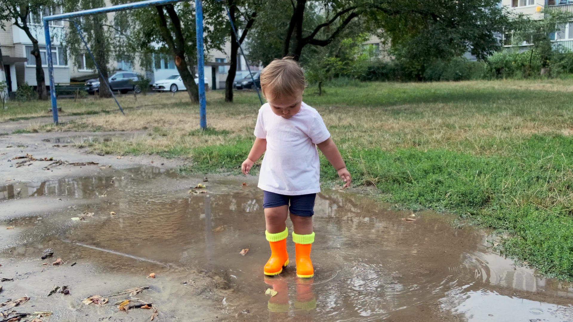 雨后穿着橙色靴子的孩子穿过水坑视频的预览图