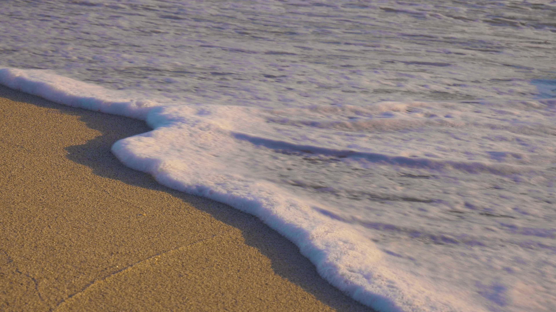 日出时海滩上有泡沫海浪近视动作缓慢视频的预览图