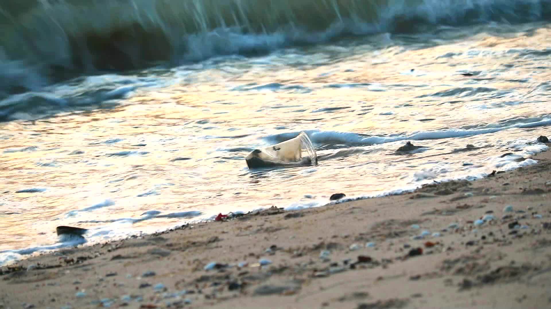 塑料玻璃和废物海浪留在海边的日落海滩上把它们吹进海里视频的预览图
