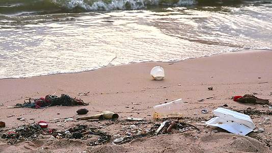 海边日落的海滩上有塑料和废物海浪把它们吹进海里视频的预览图