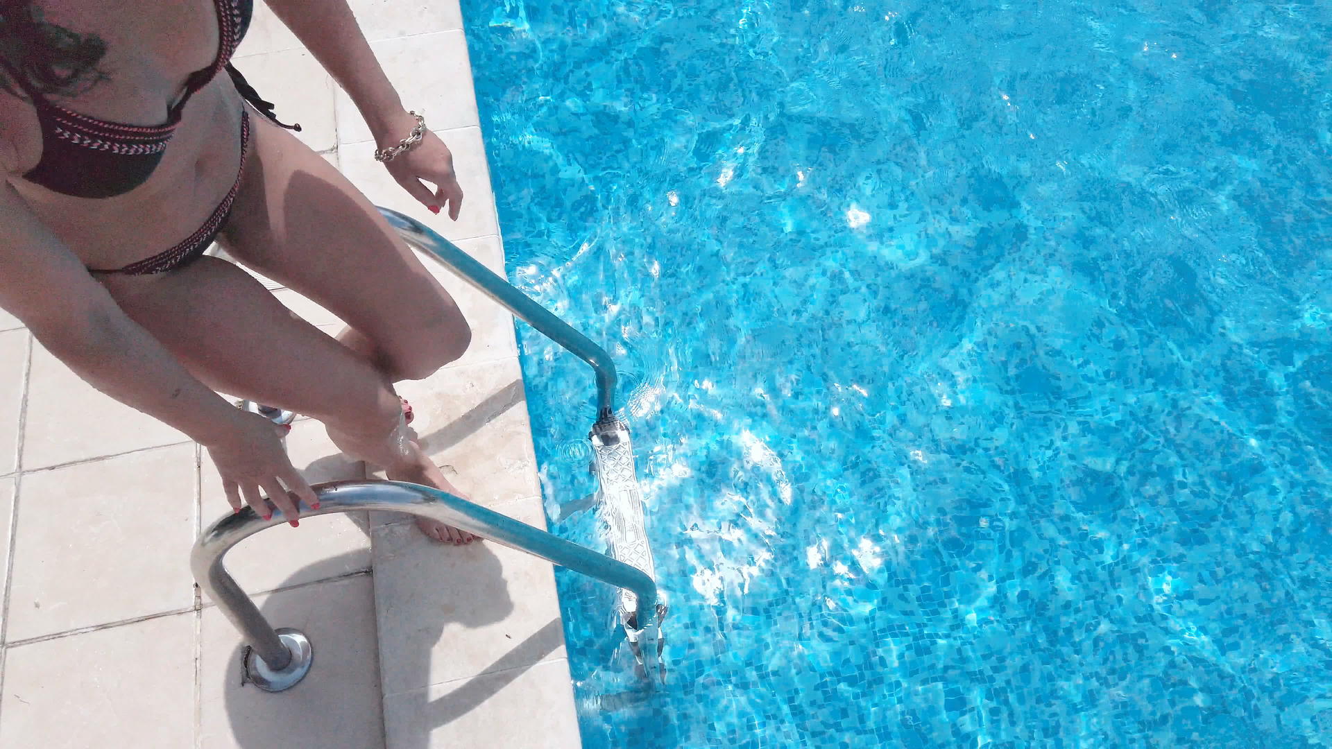 年轻女子在游泳池里通过梯子慢慢地移动视频的预览图