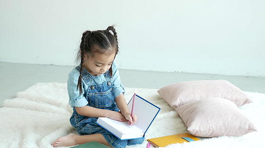当小女孩坐在地毯上和枕头旁边时她喜欢在书上写字视频的预览图