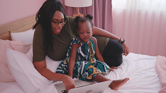 白天非裔美国母亲和女儿在床上使用笔记本电脑他们似乎视频的预览图