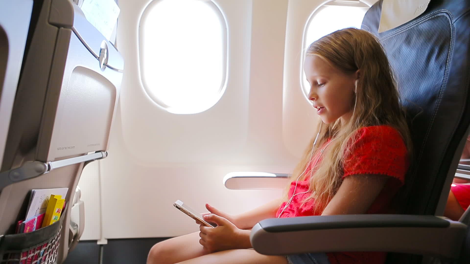 可爱的小女孩坐在飞机窗口附近的孩子们听音乐视频的预览图