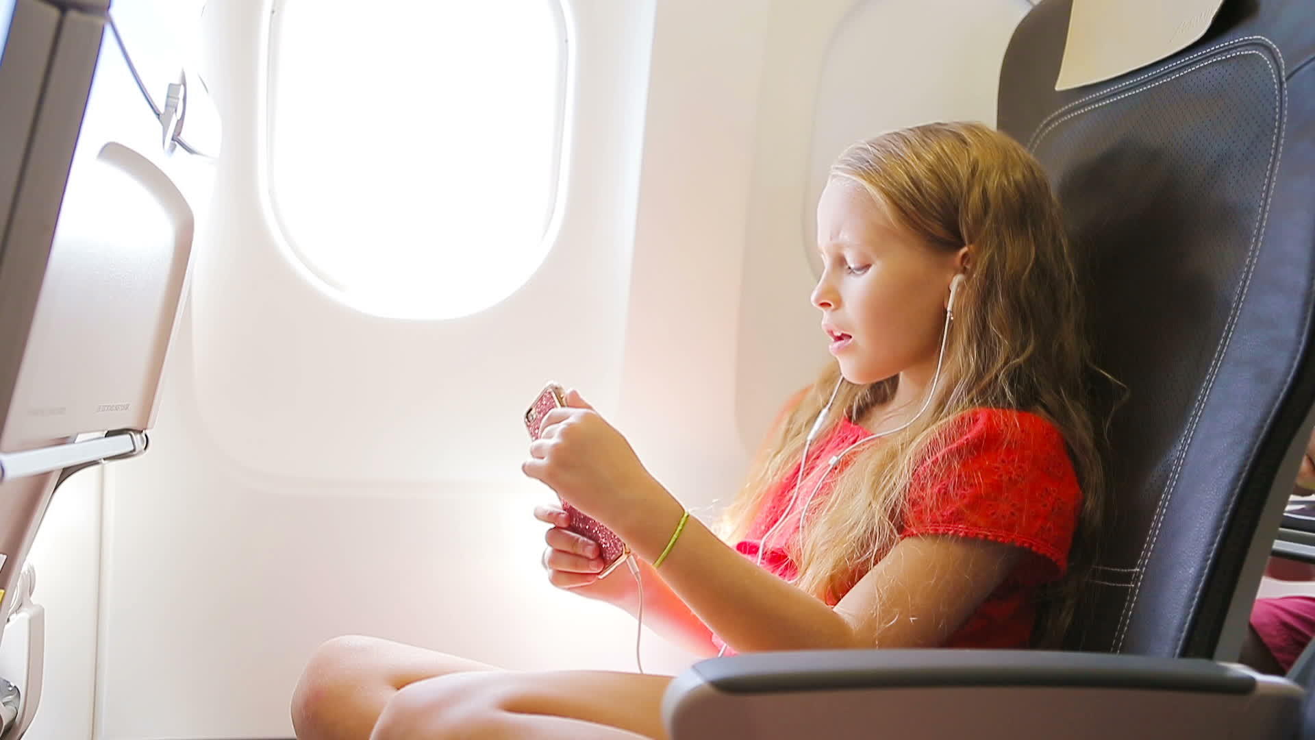 可爱的小女孩坐在飞机窗口附近的孩子们听音乐视频的预览图
