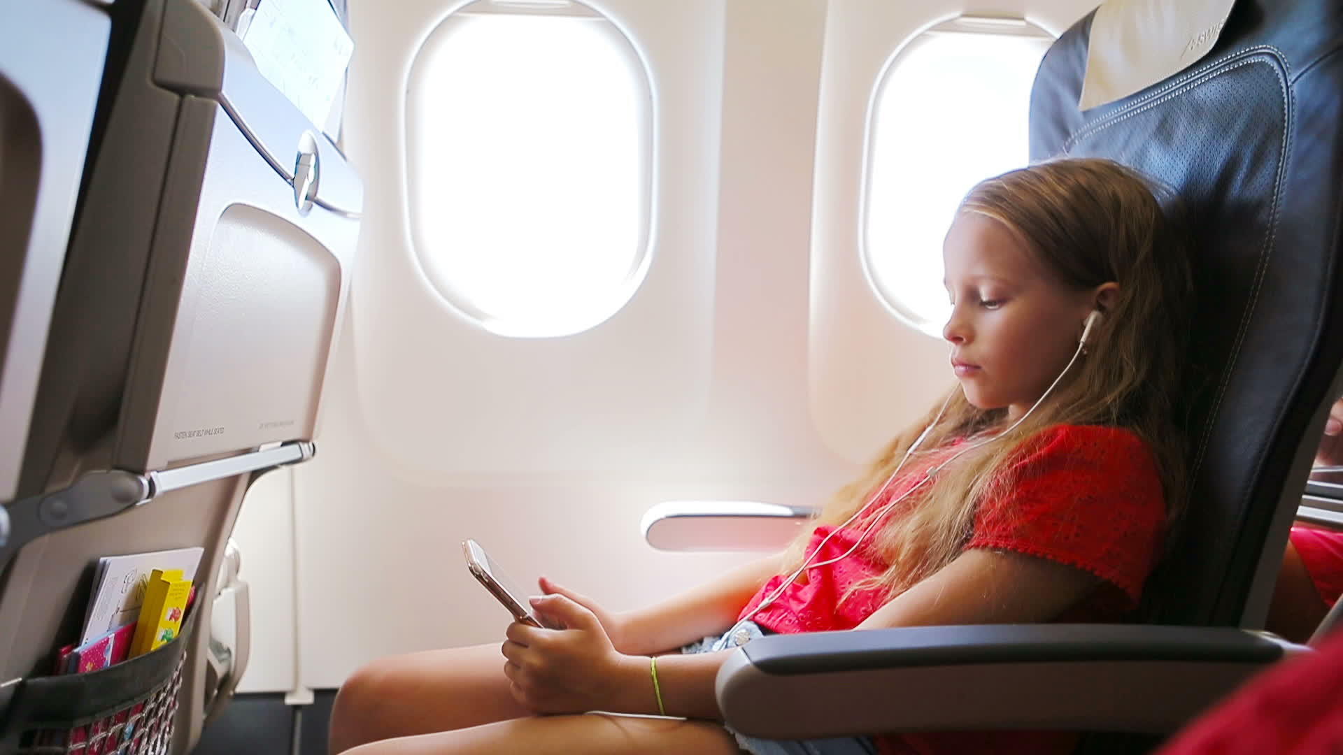 可爱的小女孩坐在窗边坐在飞机窗口附近听着可爱的小女孩的飞行视频的预览图