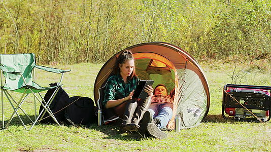 美丽的年轻女友在露营帐篷前使用平板石牌视频的预览图