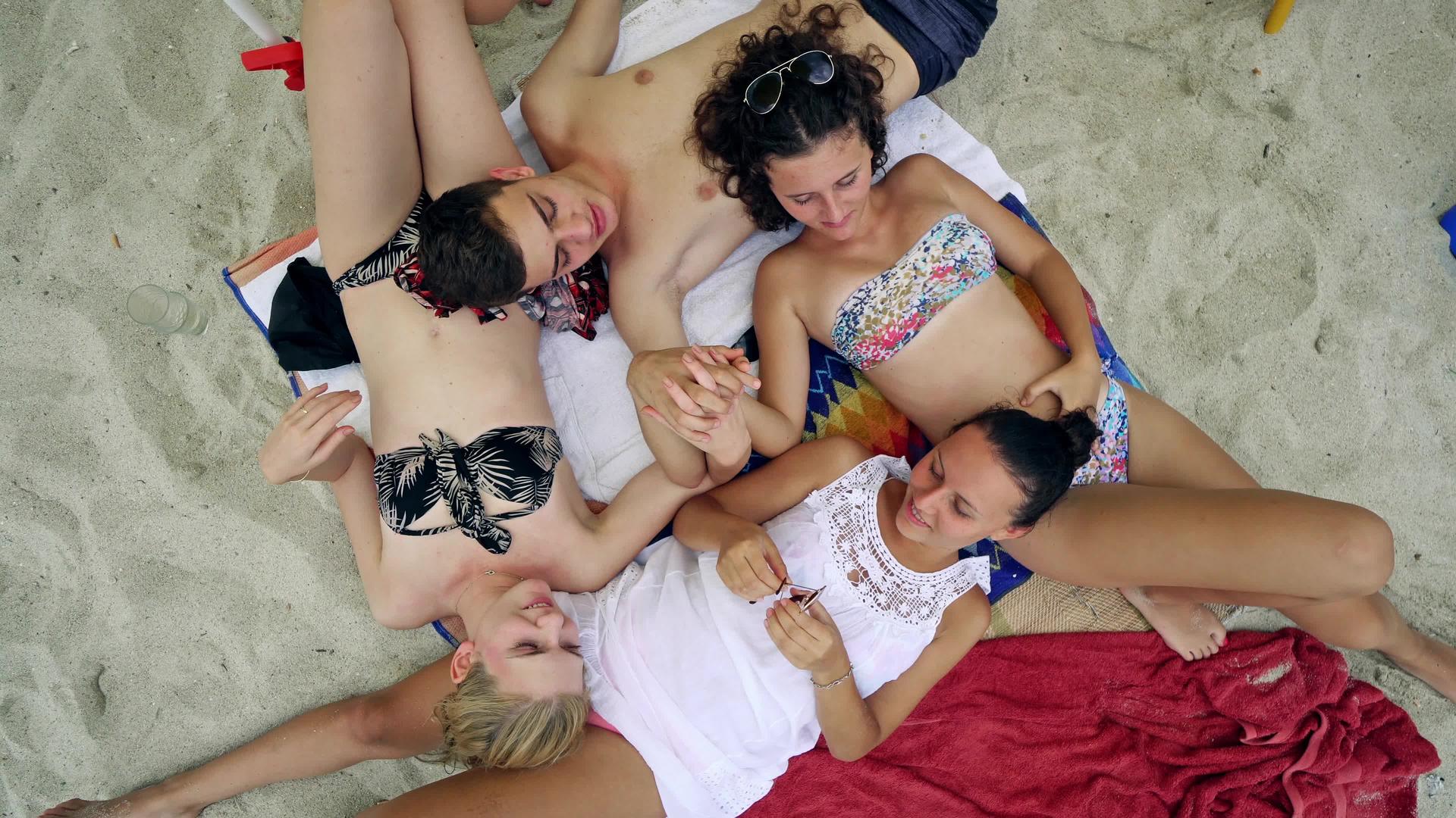 四个十几岁的朋友双手躺在海滩上视频的预览图