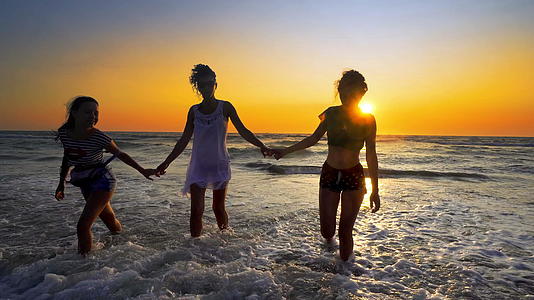 年轻女性和两个女孩在热带海滩日落时用完了视频的预览图