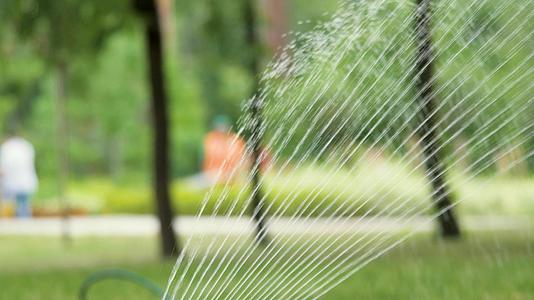 在炎热的一天园丁在浇灌草的城市公园里洒上新鲜的关闭滴水视频的预览图