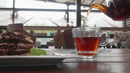 从咖啡桌上透明的茶壶里将浓茶倒入玻璃杯中夏季咖啡馆视频的预览图