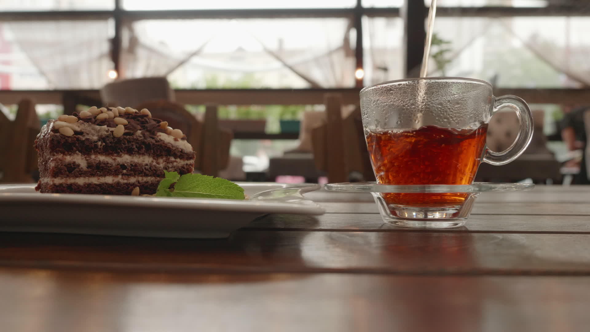 把玻璃茶壶里的热茶倒进透明的杯子里夏季咖啡馆木桌上的热茶视频的预览图