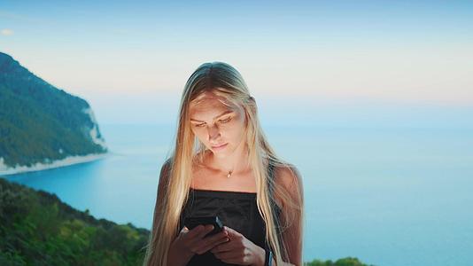 金发女性金发使用智能手机和海洋背景视频的预览图