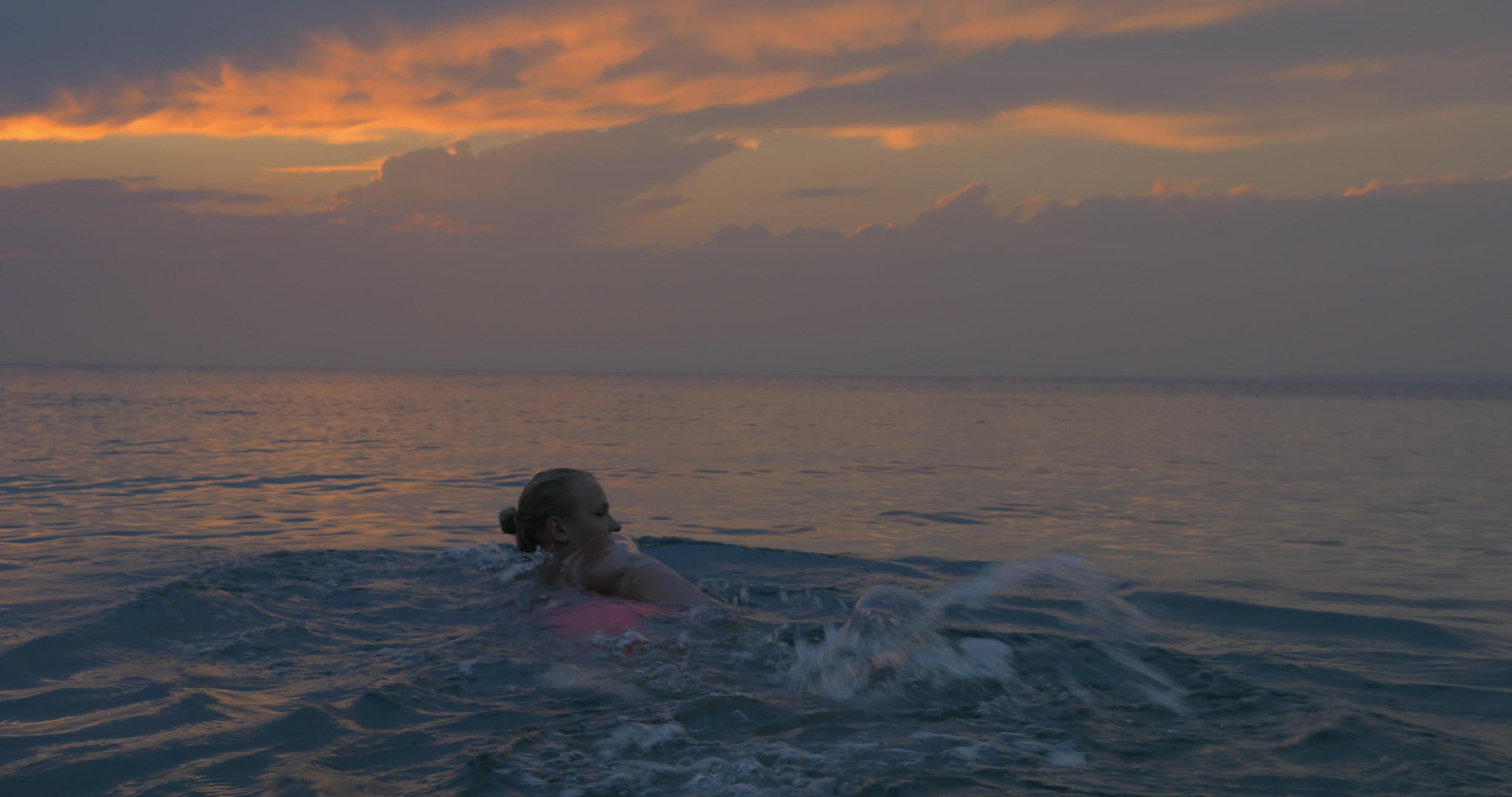 日落时分年轻女子在海中游离夜云天空平静海景平静视频的预览图