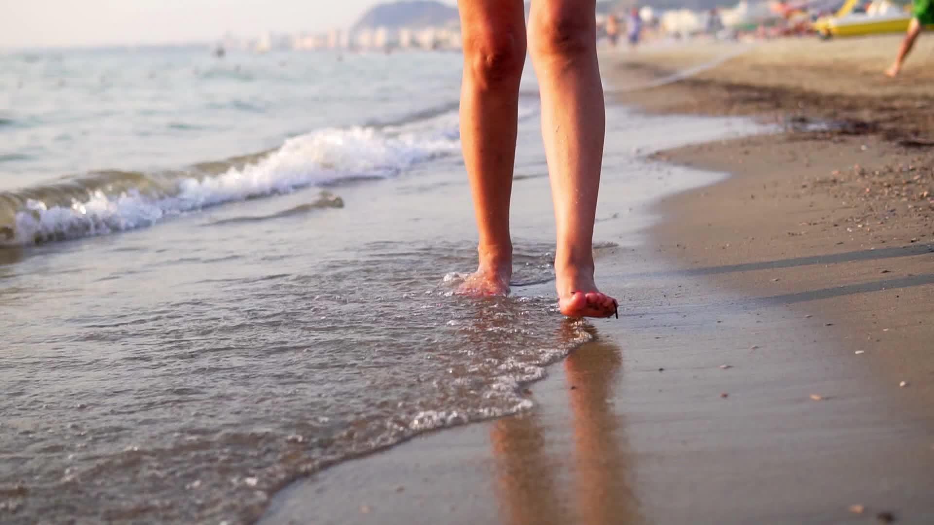 长腿的年轻女性在奇怪的沙滩上行走用慢动作喷洒海水视频的预览图
