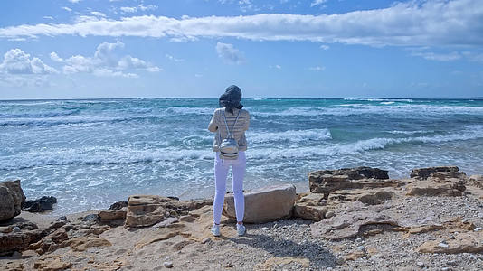 一位年轻女子站在风暴海岸的风中看着地平线视频的预览图