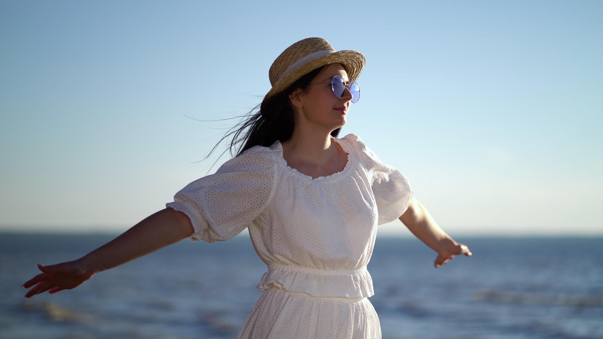 女旅行者举起双臂看着海上的草帽和白色连衣裙视频的预览图