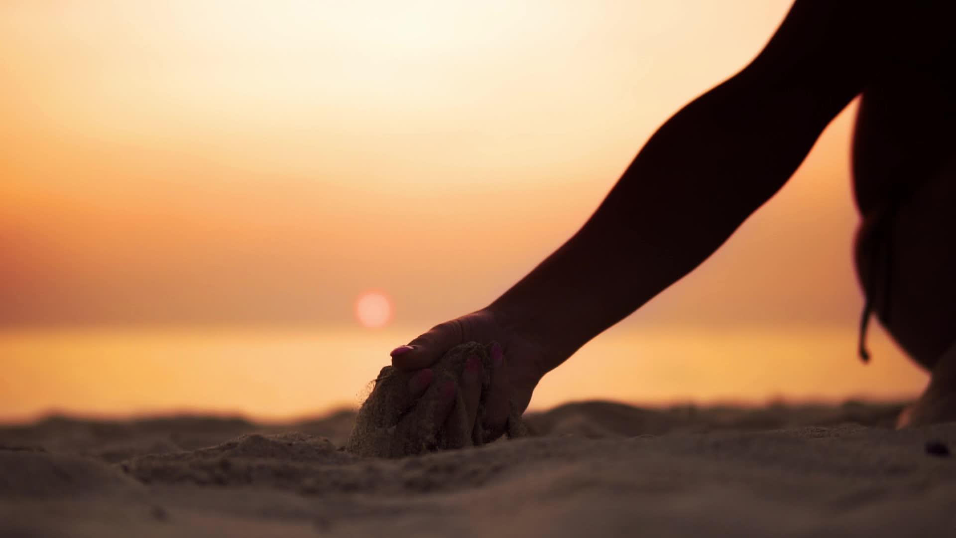 剪影手释放落沙流过手中的沙子面对橙色的海洋日落夏天视频的预览图