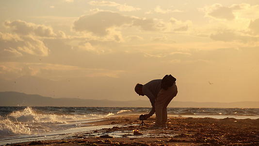 摄影师在海滩日落时拍摄自然时间和专业相机视频的预览图
