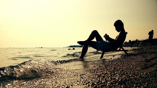 坐在椅子上的人在海滩上日落Dof上读书视频的预览图