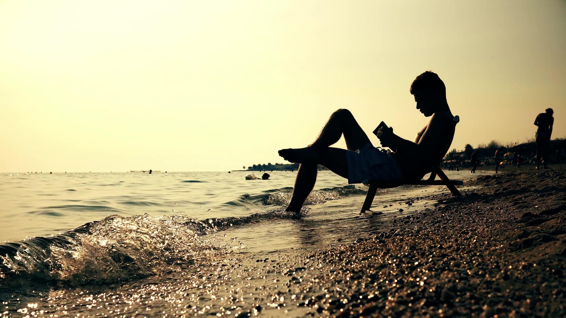 坐在椅子上的人在海滩上日落Dof上读书视频的预览图