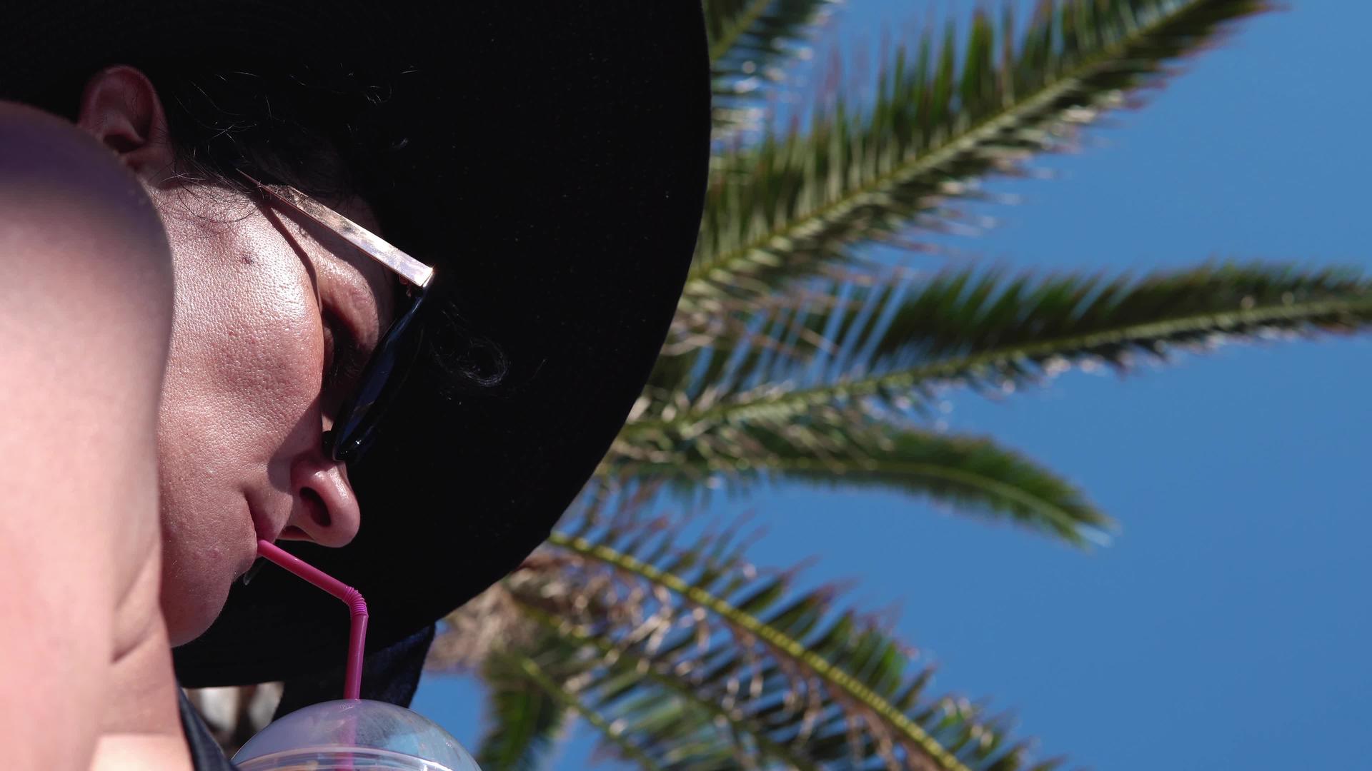 女人在棕榈树下喝鸡尾酒在热带海滩喝鸡尾酒视频的预览图