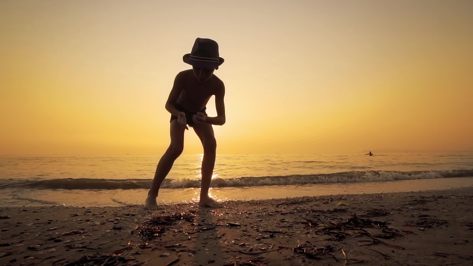男孩在海里慢慢地扔帽子和石头视频的预览图