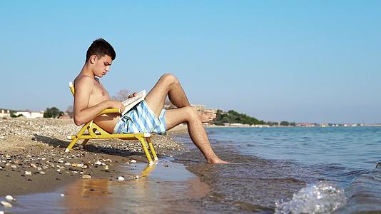 年轻人喜欢在海滩和海岸度假读一本书坐在椅子上视频的预览图