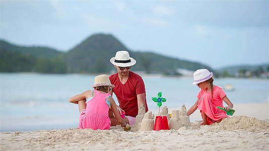 父亲和两个女孩在热带海滩上玩沙子在热带海滩上建造沙子城堡在热带海滩上建造沙子视频的预览图