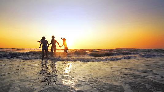 日落时在海滩上散步、跳跃和玩耍电影慢慢地从海浪中爆发出来视频的预览图