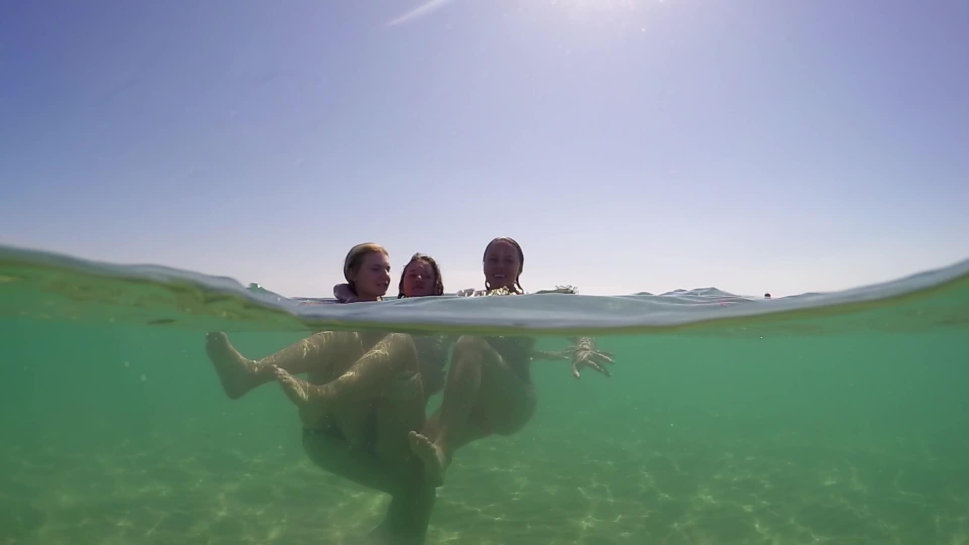 一群三个十几岁的女孩在海边的水中快乐地拥抱和飞溅视频的预览图