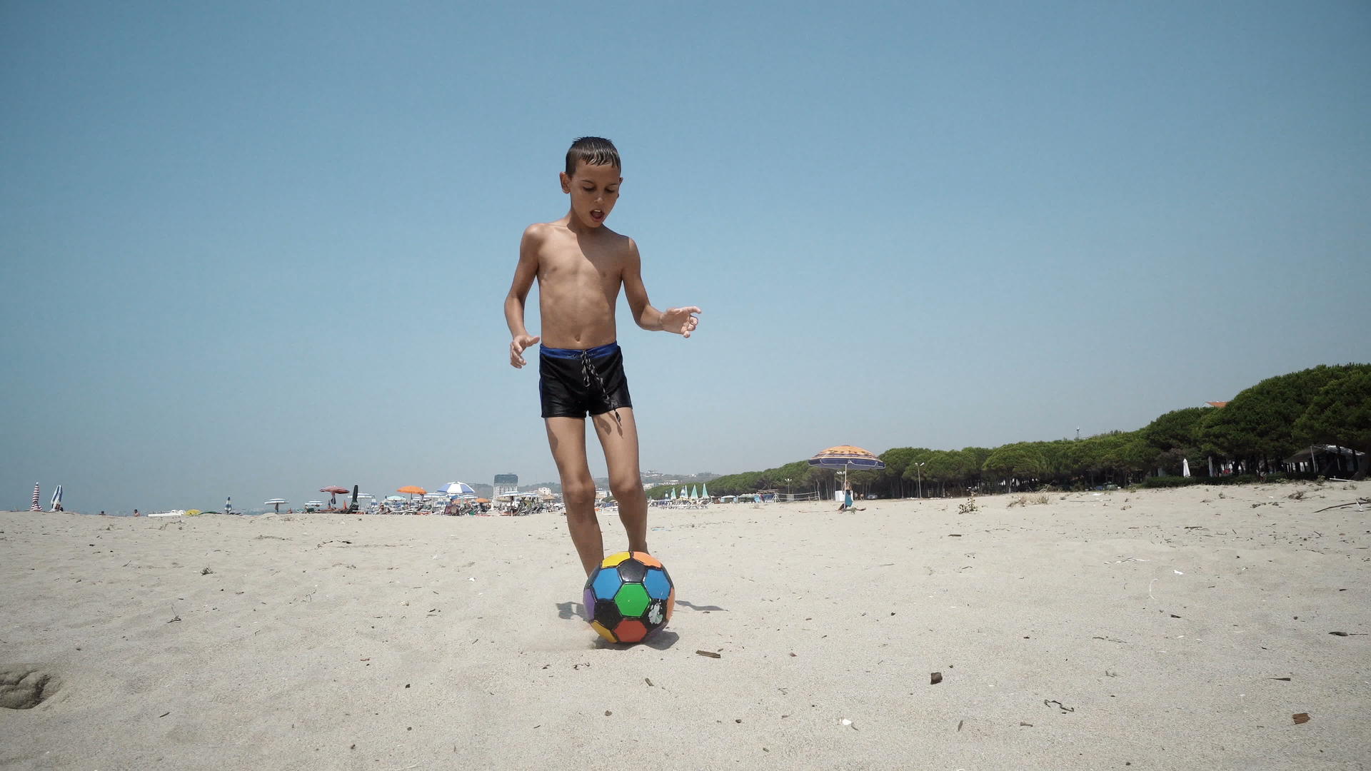年轻男孩在空荡荡的海滩上踢足球拍摄电影视频的预览图