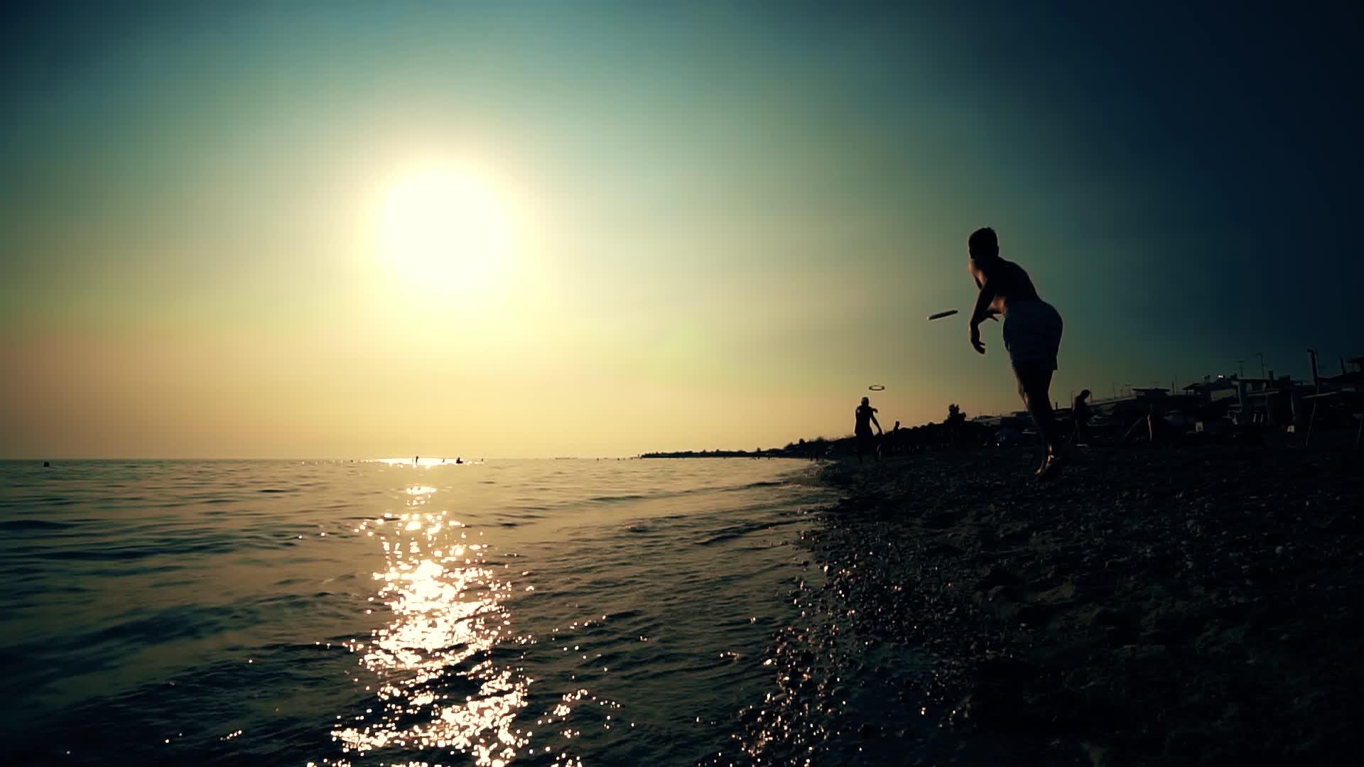 日出或日落时在海滩上玩飞盘的休眠朋友视频的预览图