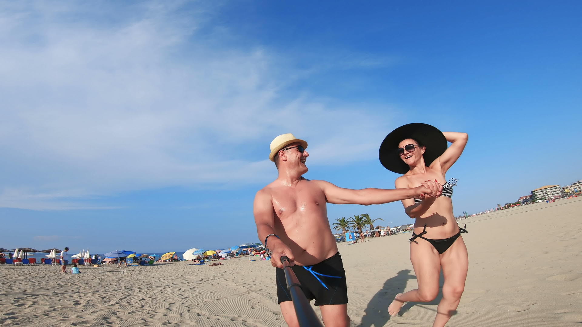 一对快乐的夫妇戴着帽子在白色海滩上奔跑视频的预览图