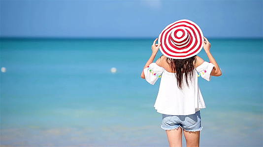 年轻美女在热带海岸玩得开心后看着海边戴帽子的女孩的风景视频的预览图