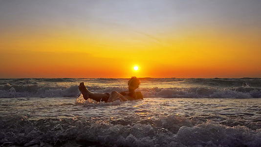 年轻微笑的女人坐在海浪中在日落时放松在暑假飞溅视频的预览图
