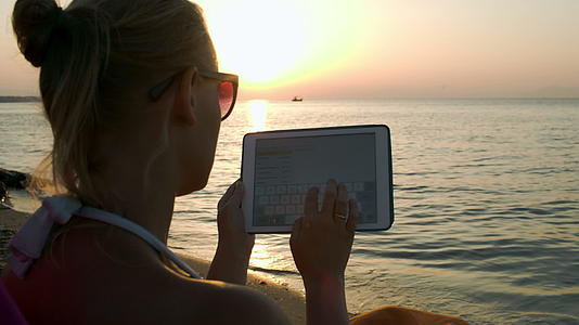 日落时坐在海边的垫子上打字视频的预览图