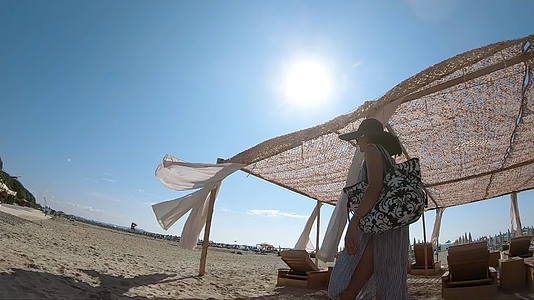 女人沿着海滩小屋走在海边的微风色的窗帘闪烁着视频的预览图