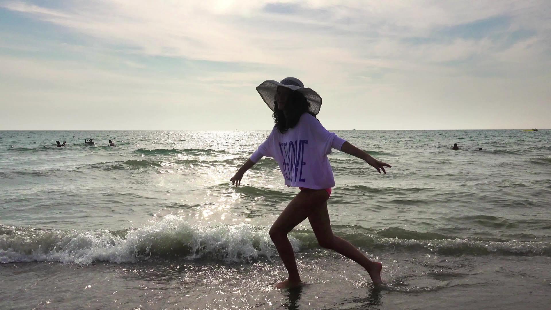 快乐的女孩享受在海滩上散步的自由伸展和跳跃被海浪溅起视频的预览图