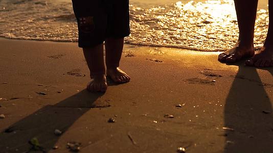 日落时婴儿和孩子们在海边的沙滩上走来走去慢慢地关上脚视频的预览图