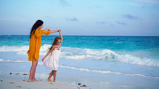 可爱的小女孩和年轻的母亲在温暖的夜晚在热带海滩日落视频的预览图