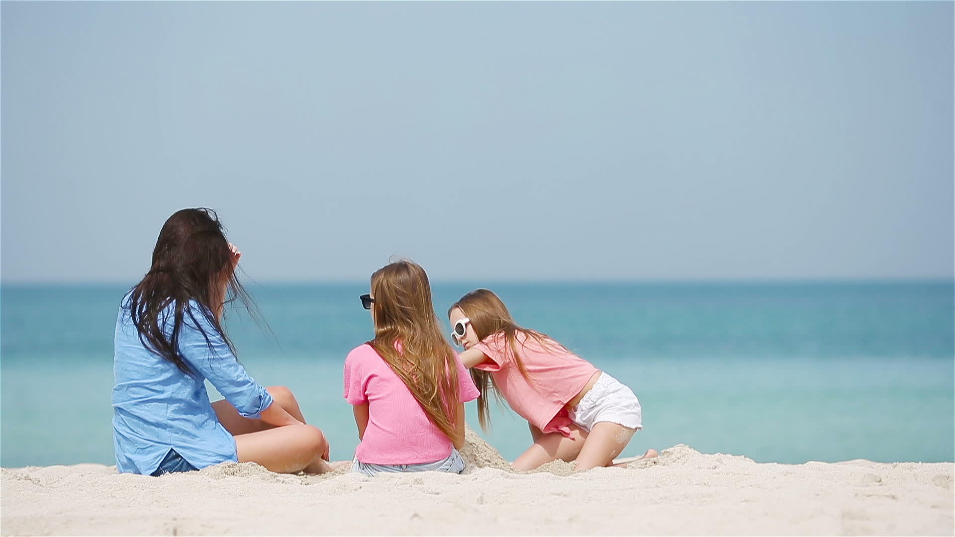 母亲和小女儿在热带海滩建造沙城堡视频的预览图