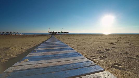 日出时走在金色沙滩的木地板上视频的预览图